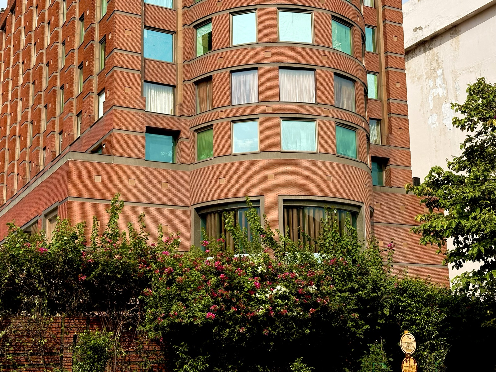Curved red-brick building behind flowering trees