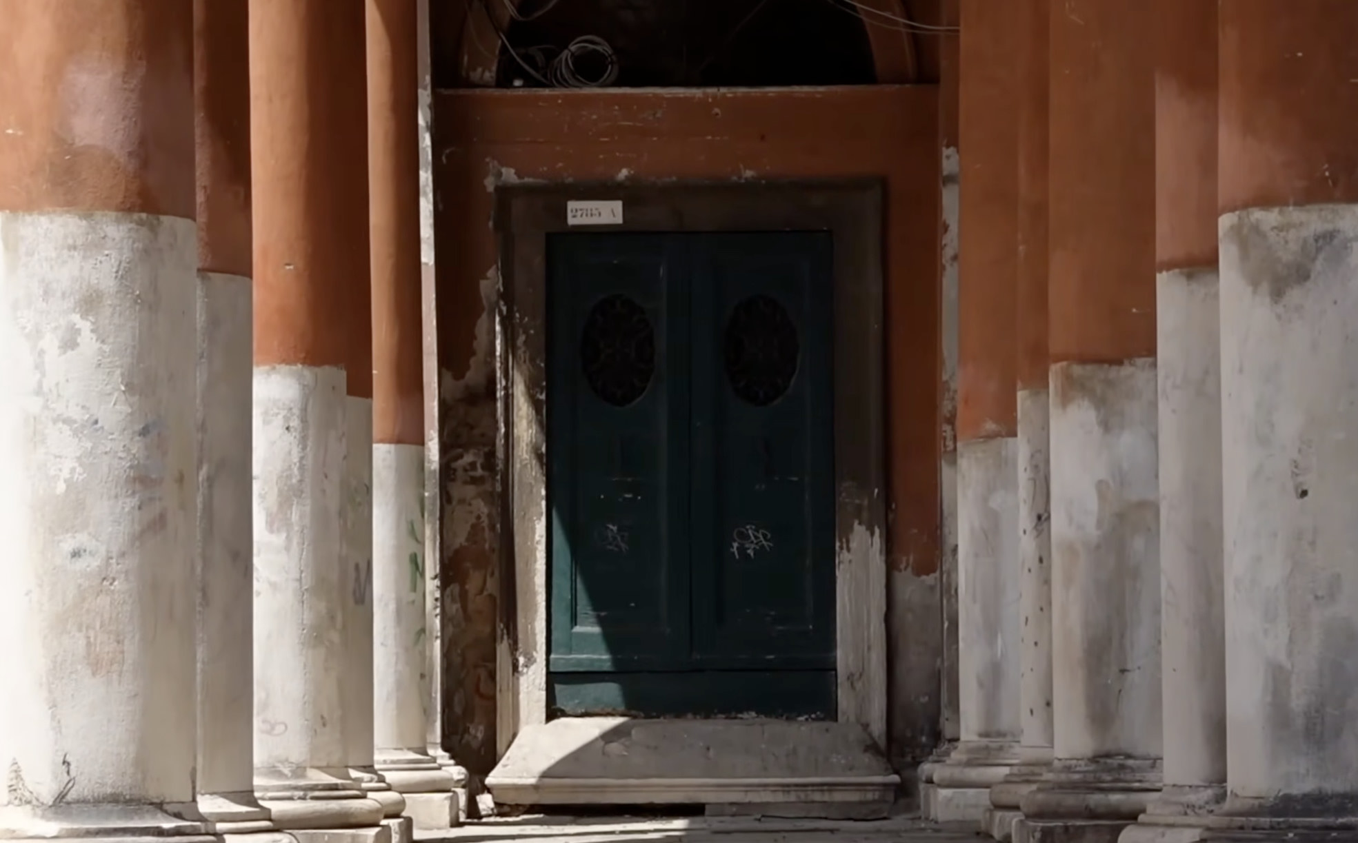 Weathered green door set between peeling terracotta columns