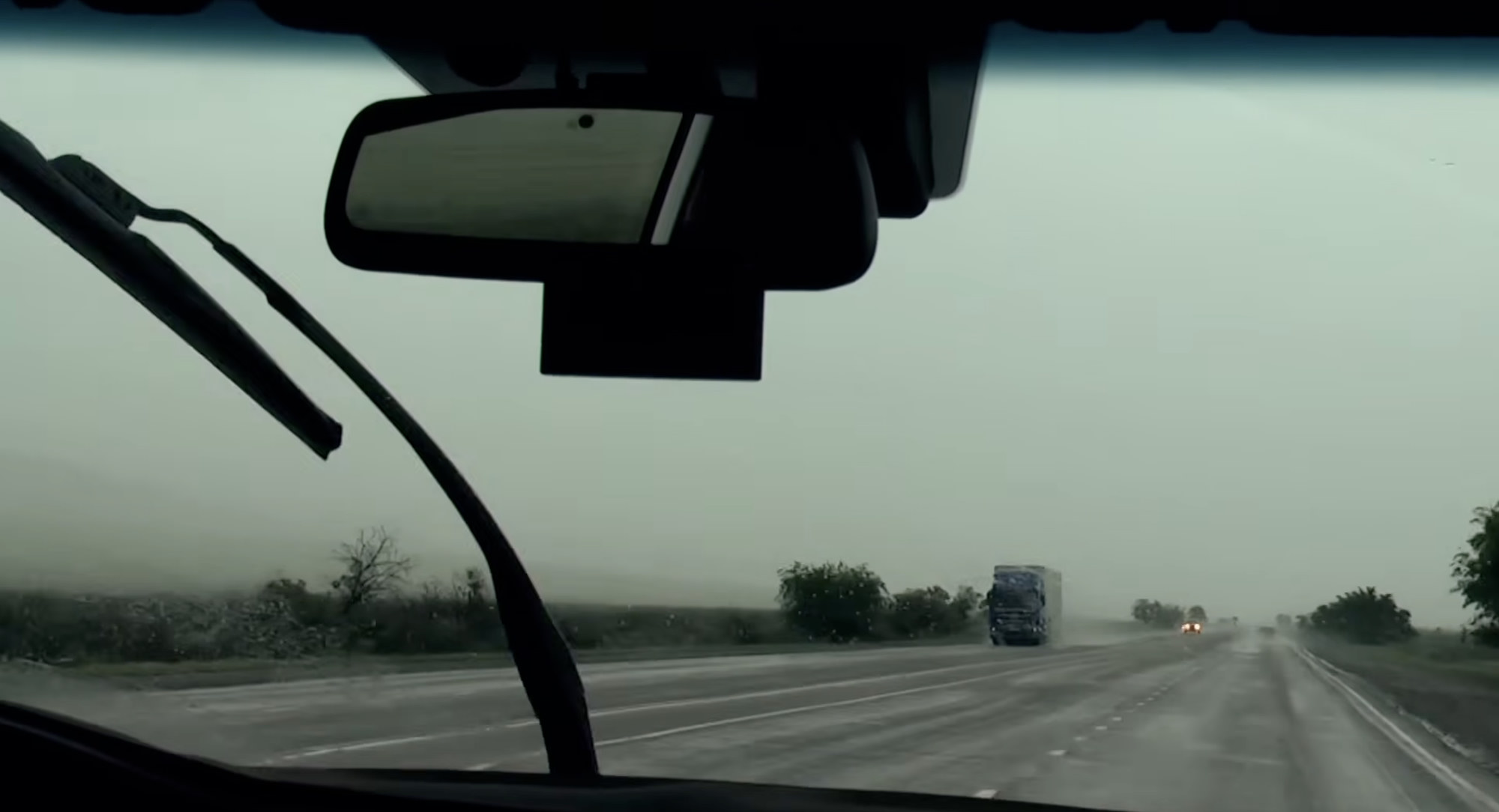 View from a car windshield of a wet highway and a truck in the distance