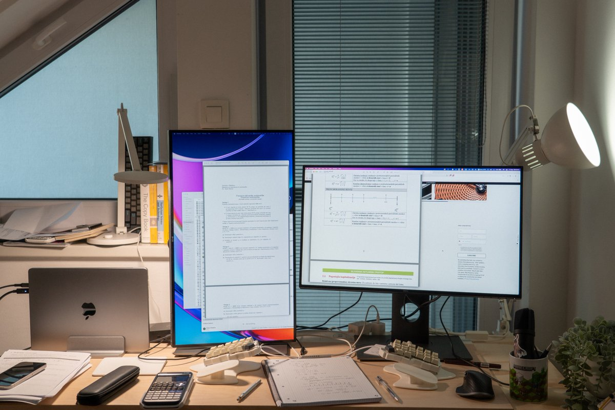 A warm study desk with multiple monitors, books, and a laptop