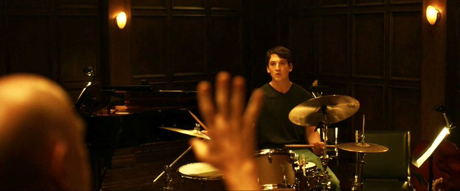 A drummer in a dark room seen from behind a raised hand